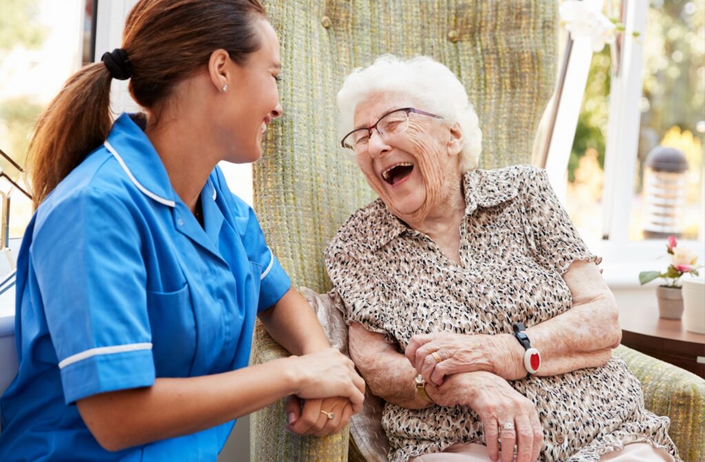 An older adult woman in a senior living facility sitting on a chair smiling and having a conversation with a nurse