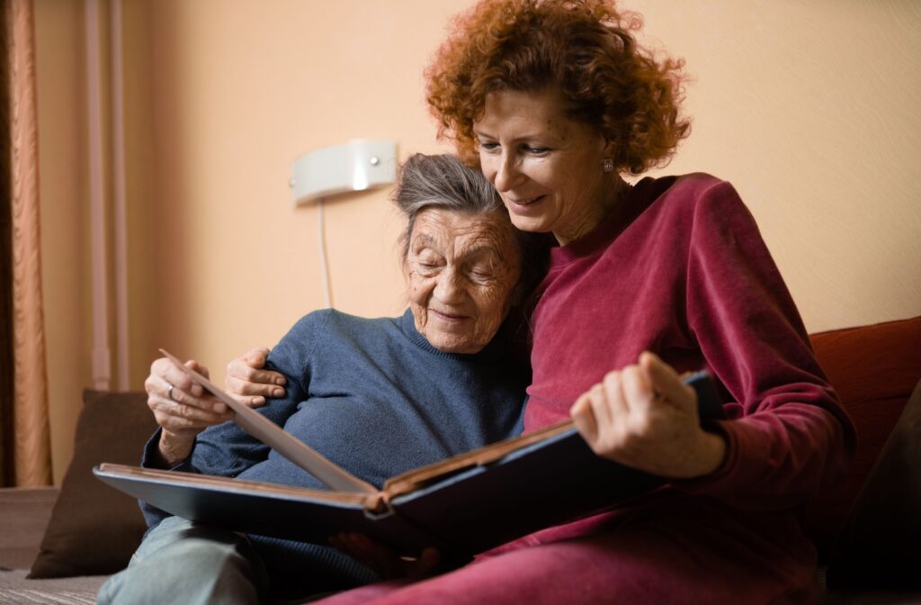 An older adult woman and her daughter smiling while looking at a photo album together.
